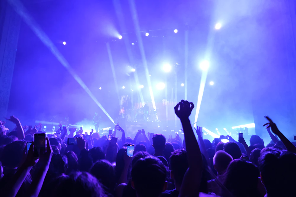Concertgoers raising their hands beneath blue stage lights