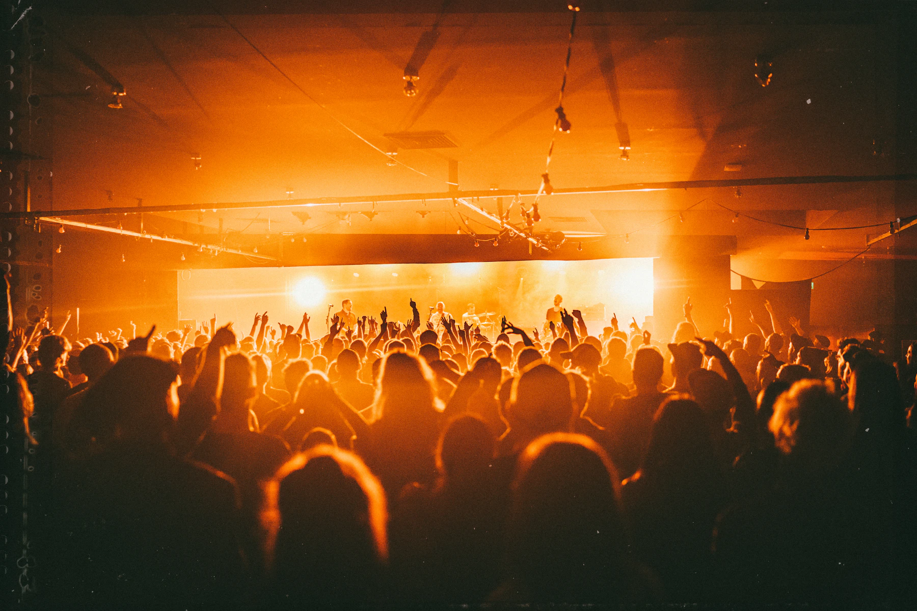 A crowd with raised hands at a live show, lit by warm amber stage lights